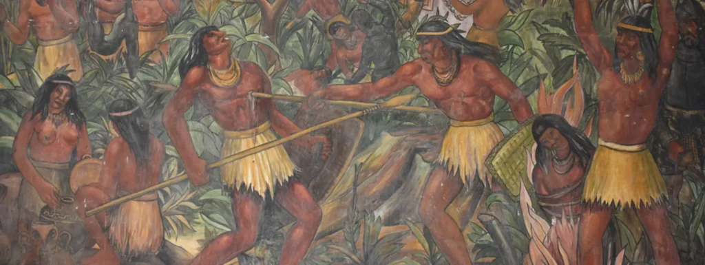 Mural que ilustra a varios indígenas luchando entre sí con lanzas en una escena de conflicto, destacando el choque que emergió entre la cultura española y la cultura indinena, donde algunos indígenas luchaban por la corona española. rodeados de un entorno selvático