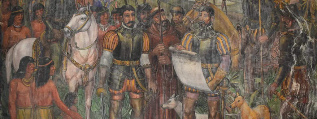 Mural que muestra a los conquistadores españoles junto a un grupo de indígenas, con uno de los conquistadores montado en un caballo y otros mostrando un documento, representando el encuentro entre los colonizadores y las culturas nativas en el período de la conquista.